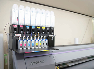 ▲ 「JV100-160」では「AS5」インクを使用。バルクインク供給システム（2ℓ）を採用し、連日の出力業務に対応している。同機は生産重視の4色モデルのほか、8色も対応可能。