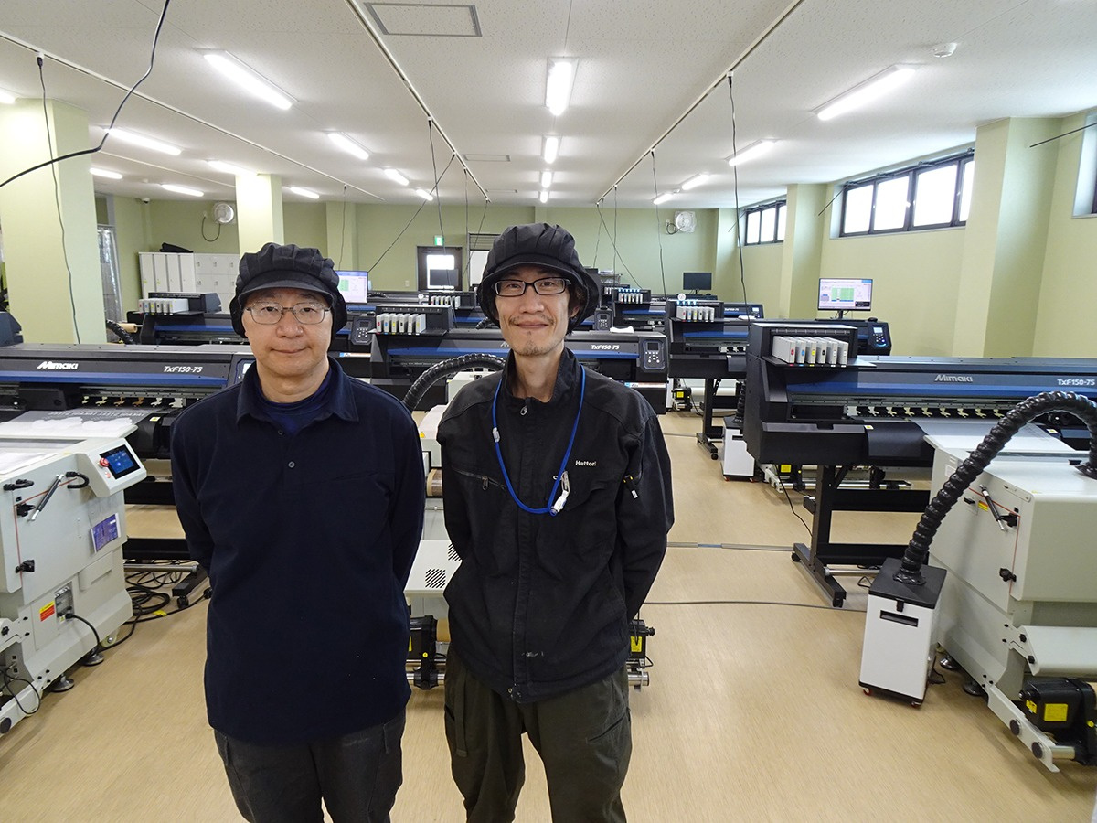 多度工場4階の物販部門には11台のTxF150-75が並ぶ（多度工場スタッフと）